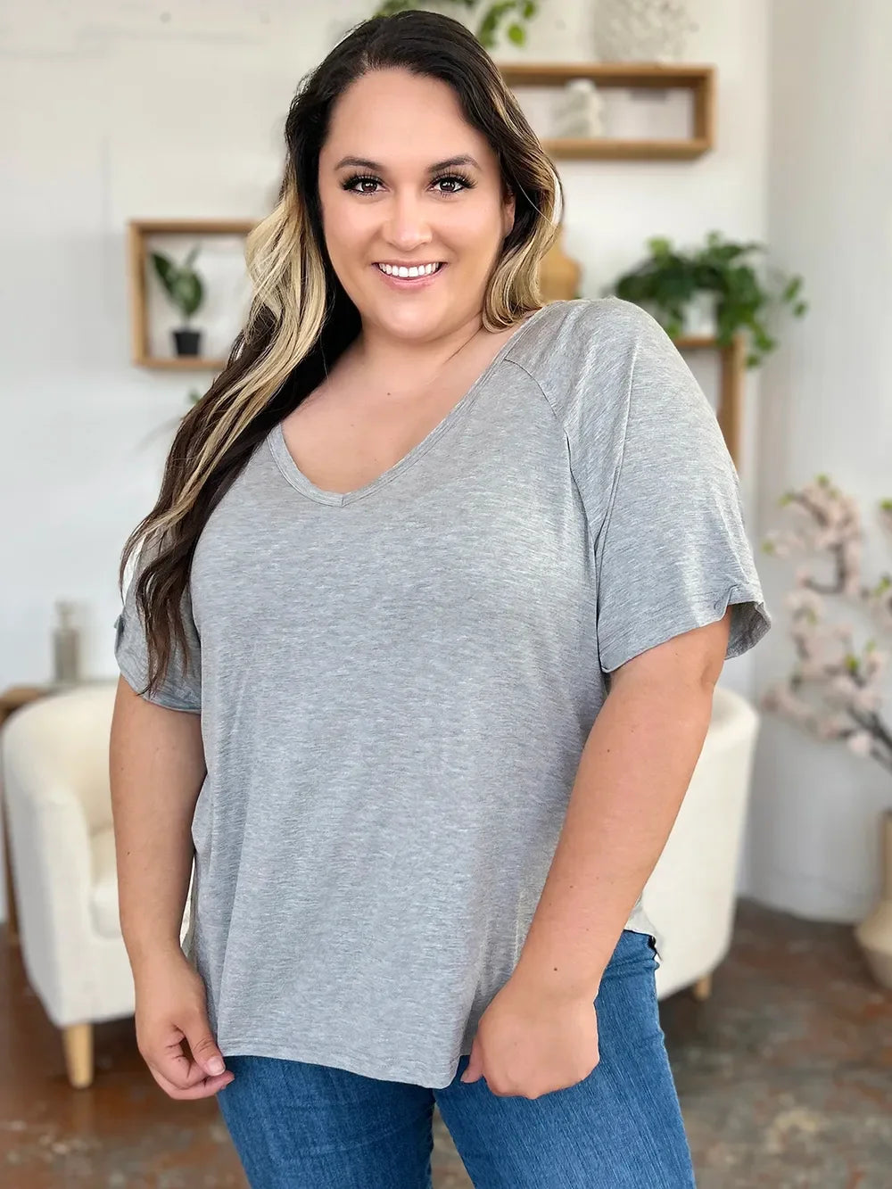 Smiling woman wearing a casual grey short-sleeve V-neck top and blue jeans indoors