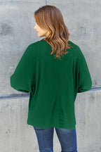 Woman in green long-sleeve top and jeans standing against a concrete wall