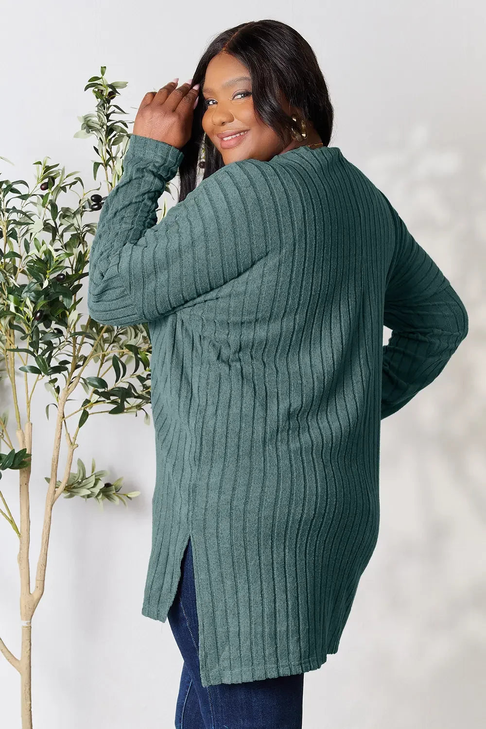 Woman modeling a ribbed teal long sleeve sweater and dark jeans, smiling indoors