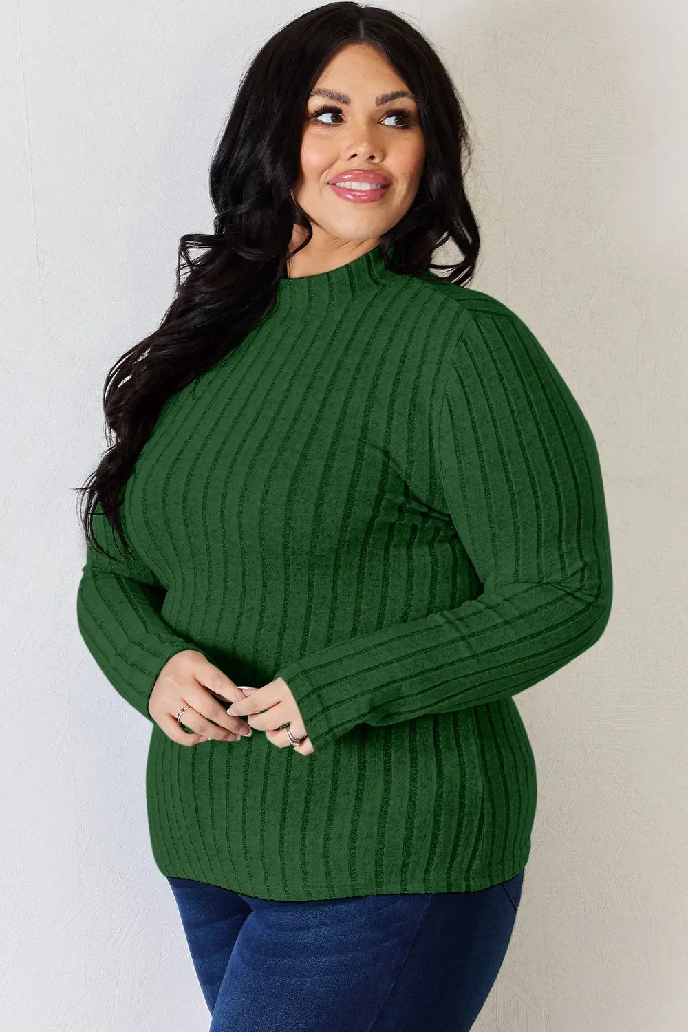 Woman in long sleeve green ribbed sweater and blue jeans posing indoors