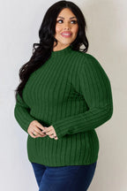 Woman in long sleeve green ribbed sweater and blue jeans posing indoors