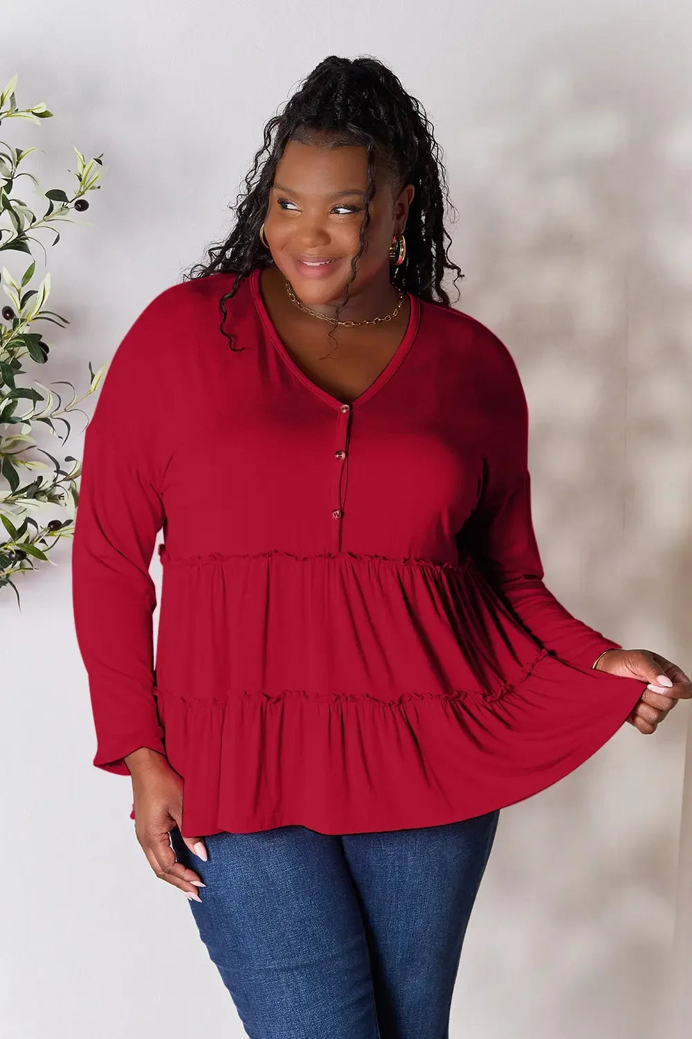 Plus size woman in a red tiered long sleeve blouse and blue jeans, smiling indoors