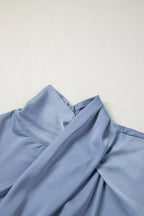 Light blue satin blouse with draped high neck and gathered details on neutral background