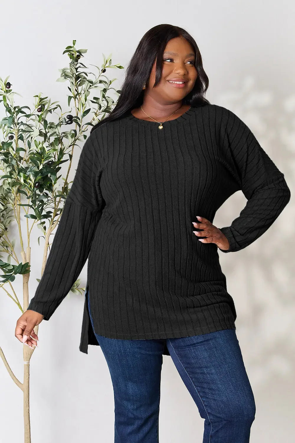 Woman modeling a black ribbed knit sweater with long sleeves and blue jeans, casual outfit