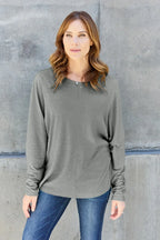 Woman in grey long sleeve top and blue jeans standing against concrete wall