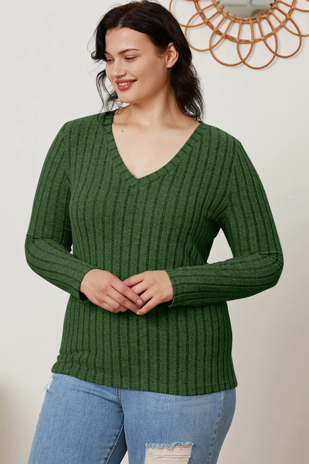 Woman wearing a green ribbed V-neck long sleeve sweater with light ripped jeans.