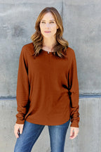 Woman wearing a brown long sleeve sweater and blue jeans against concrete wall