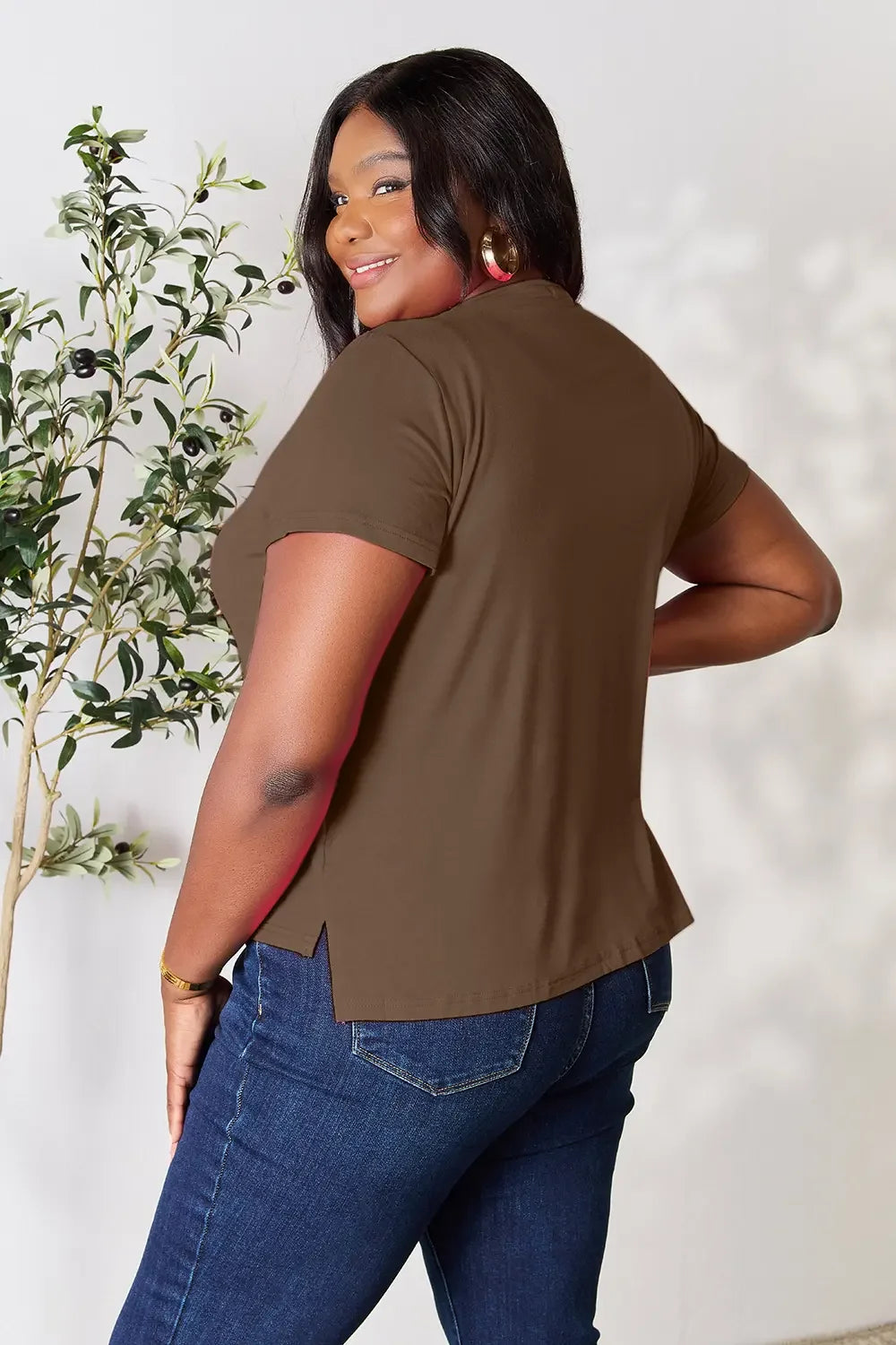 Smiling woman in a brown short sleeve top and blue jeans, casual fashion, indoor setting.