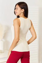 Woman wearing a sleeveless cream ribbed top and red pants in a modern indoor setting
