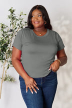 Plus size woman wearing a grey short sleeve t-shirt and blue jeans, standing by a plant.