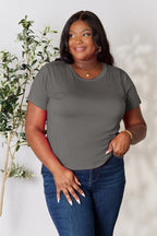 Woman in gray short sleeve t-shirt and blue jeans, standing by green indoor plant