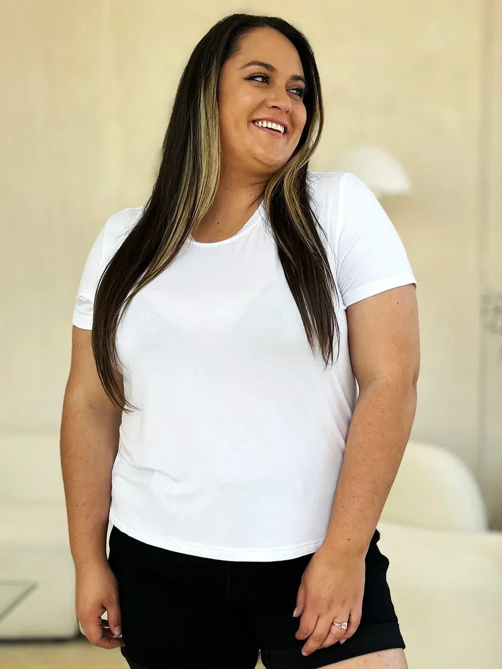 Smiling woman in a white t-shirt and black shorts standing indoors, casual fashion