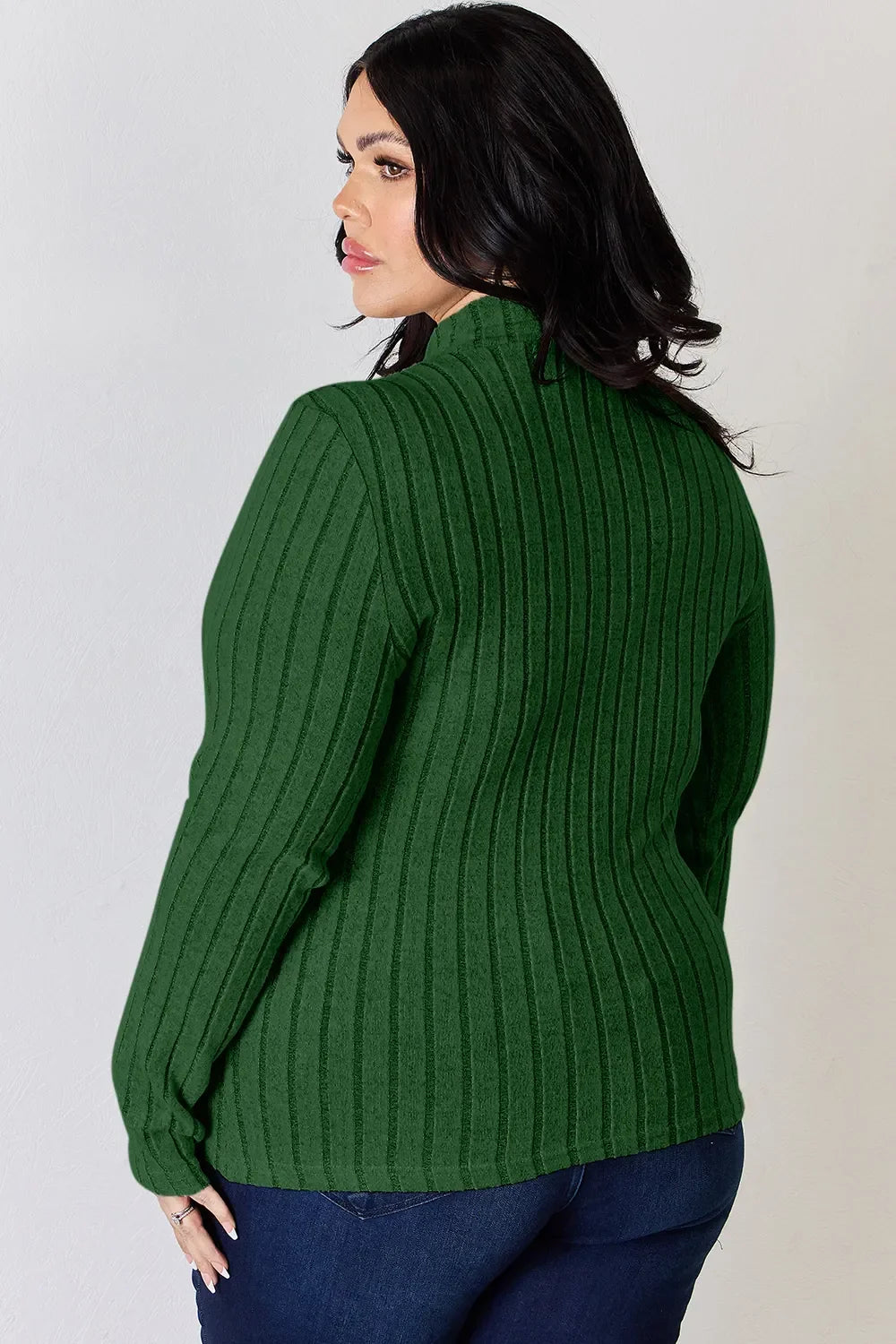 Woman wearing a ribbed green long sleeve sweater and blue jeans, side view
