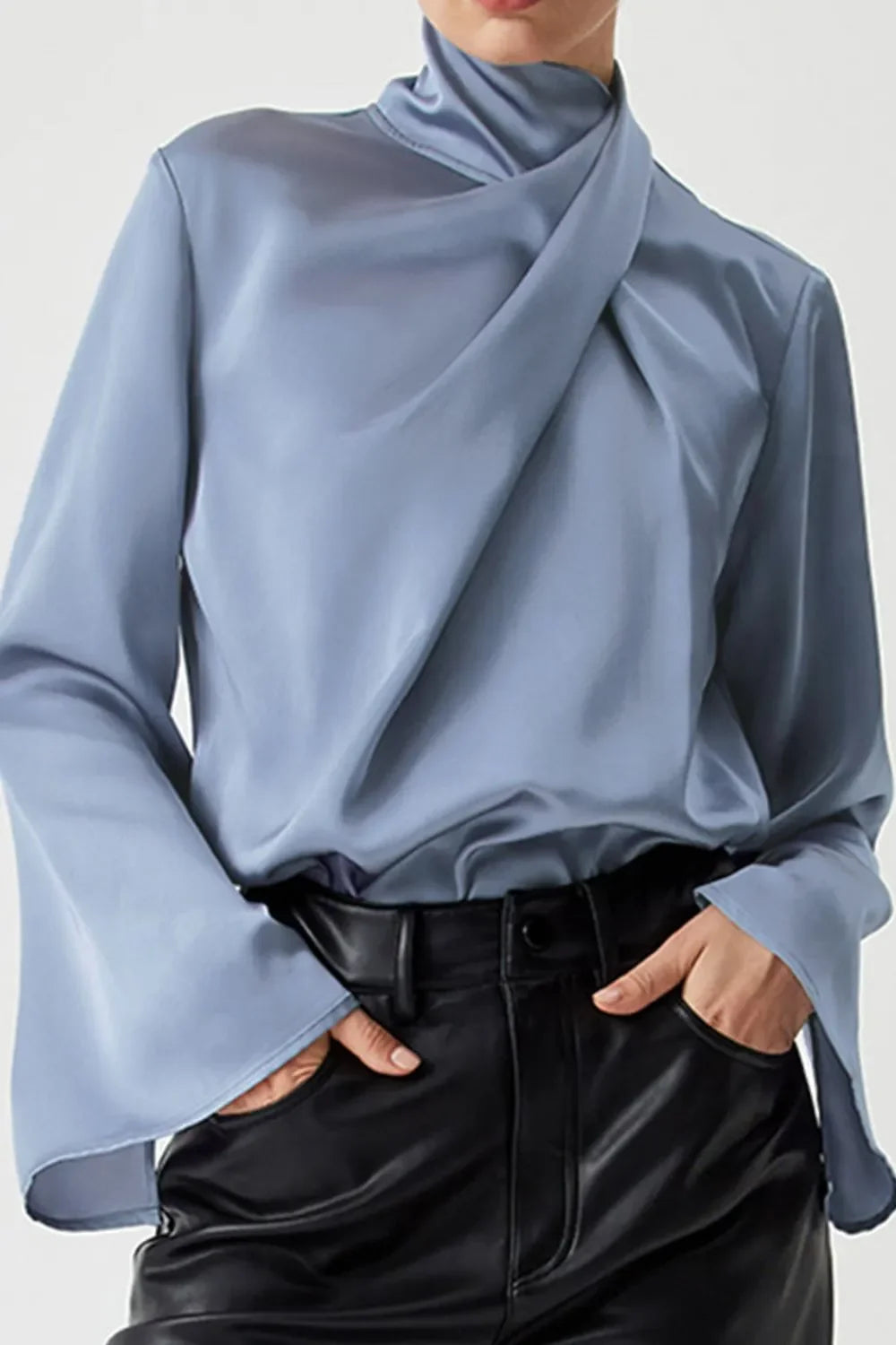 Woman wearing light blue satin blouse with draped neckline and black faux leather pants