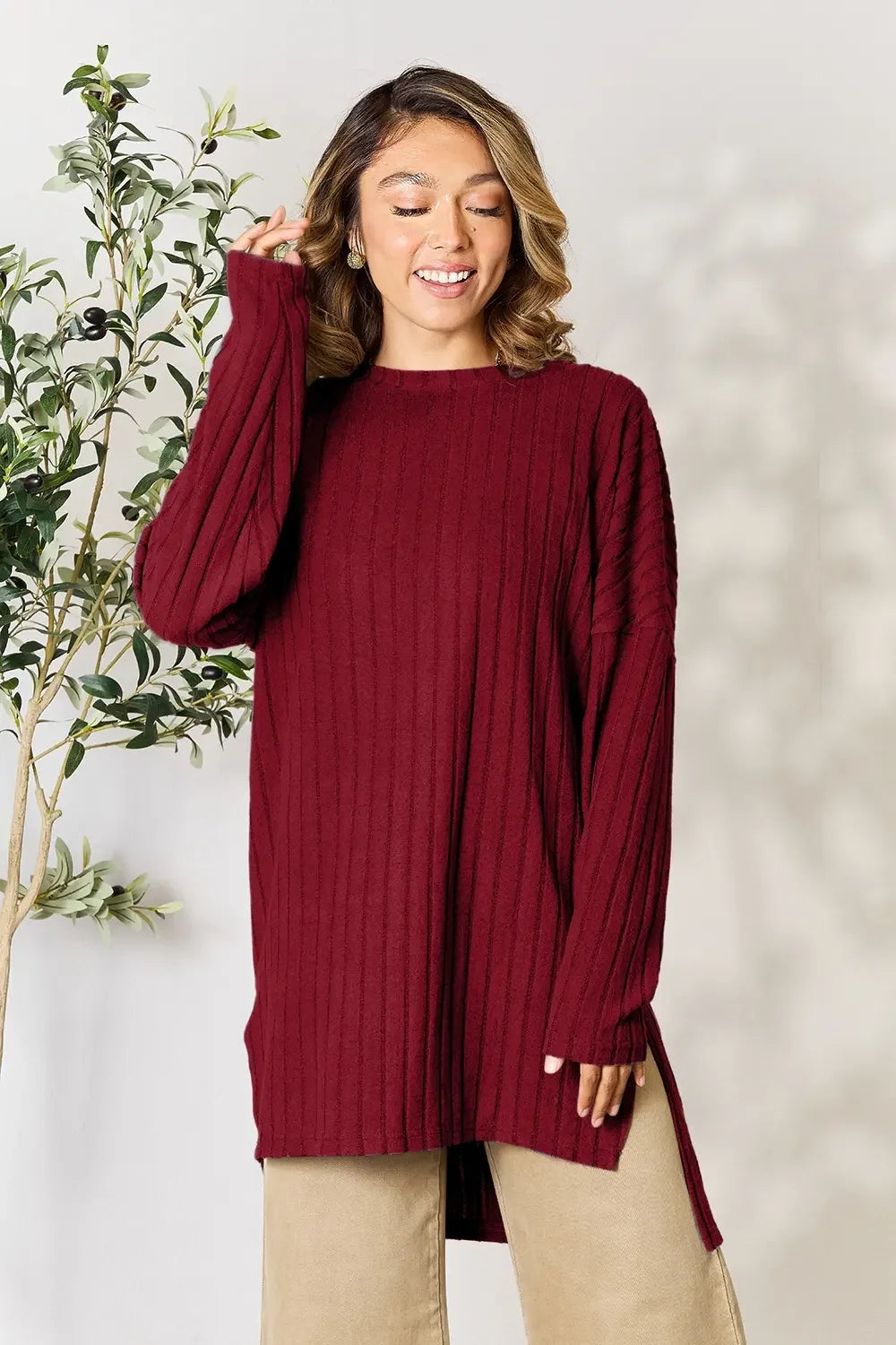 Woman wearing a long sleeve ribbed burgundy sweater tunic and beige pants standing indoors