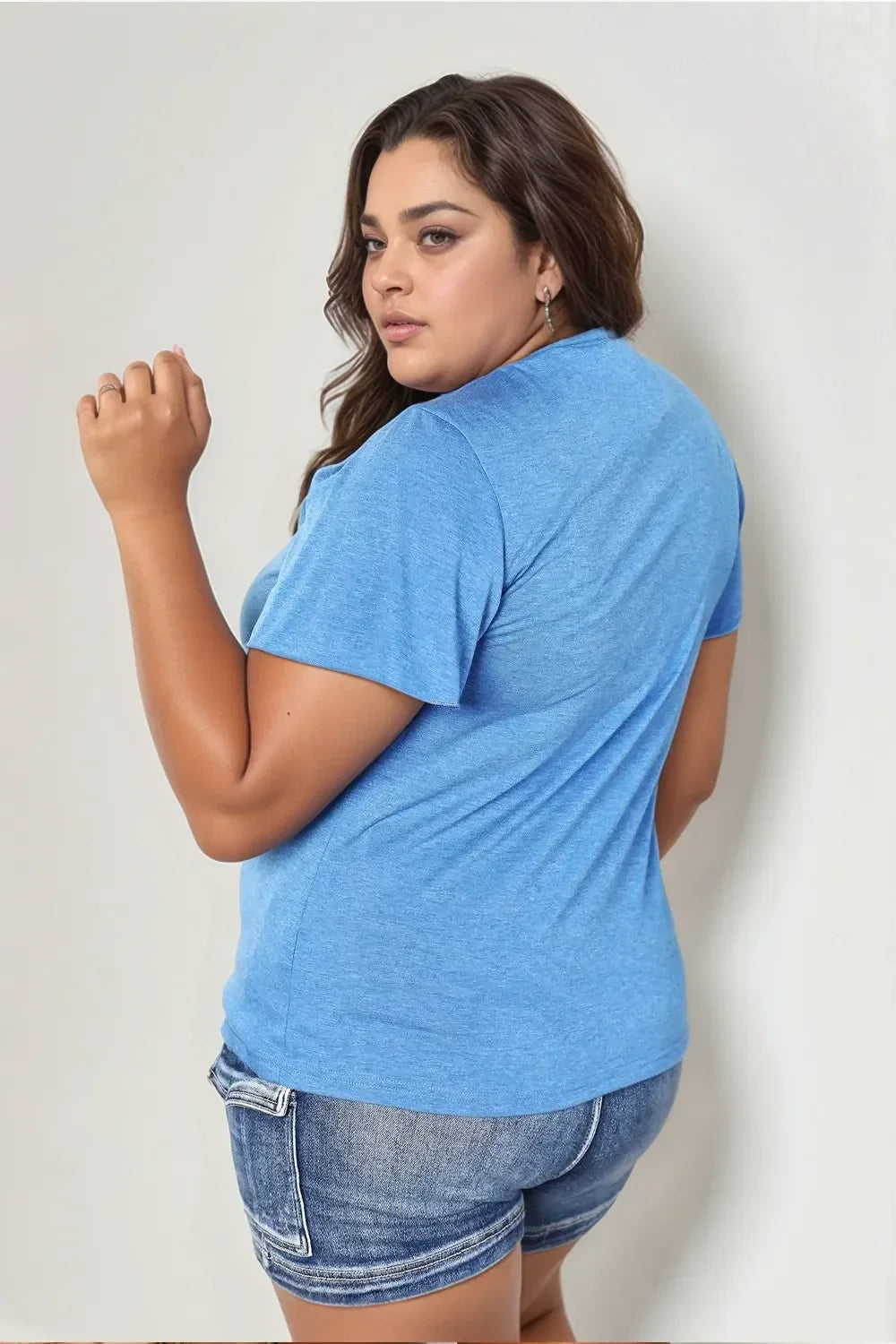 Woman in a blue t-shirt and denim shorts posing against a light background
