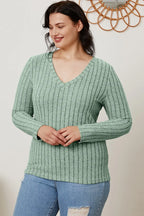 Woman wearing a green striped V-neck long sleeve sweater and ripped blue jeans
