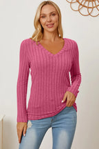 Woman wearing a pink ribbed V-neck sweater and distressed light blue jeans
