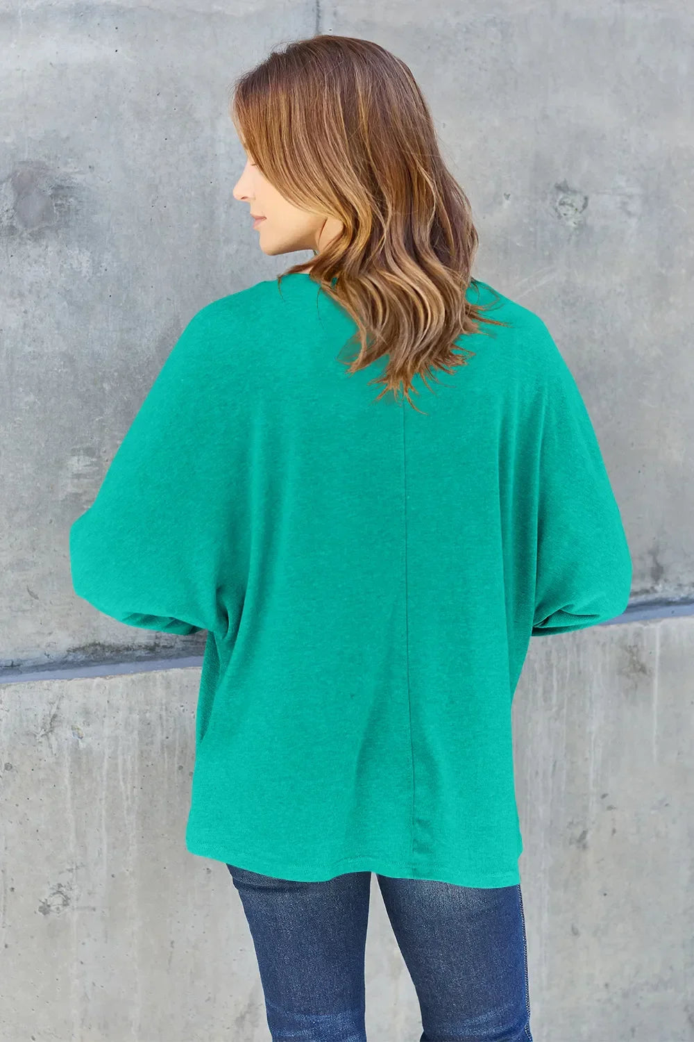 Woman in casual green sweater and jeans standing against concrete wall, back view