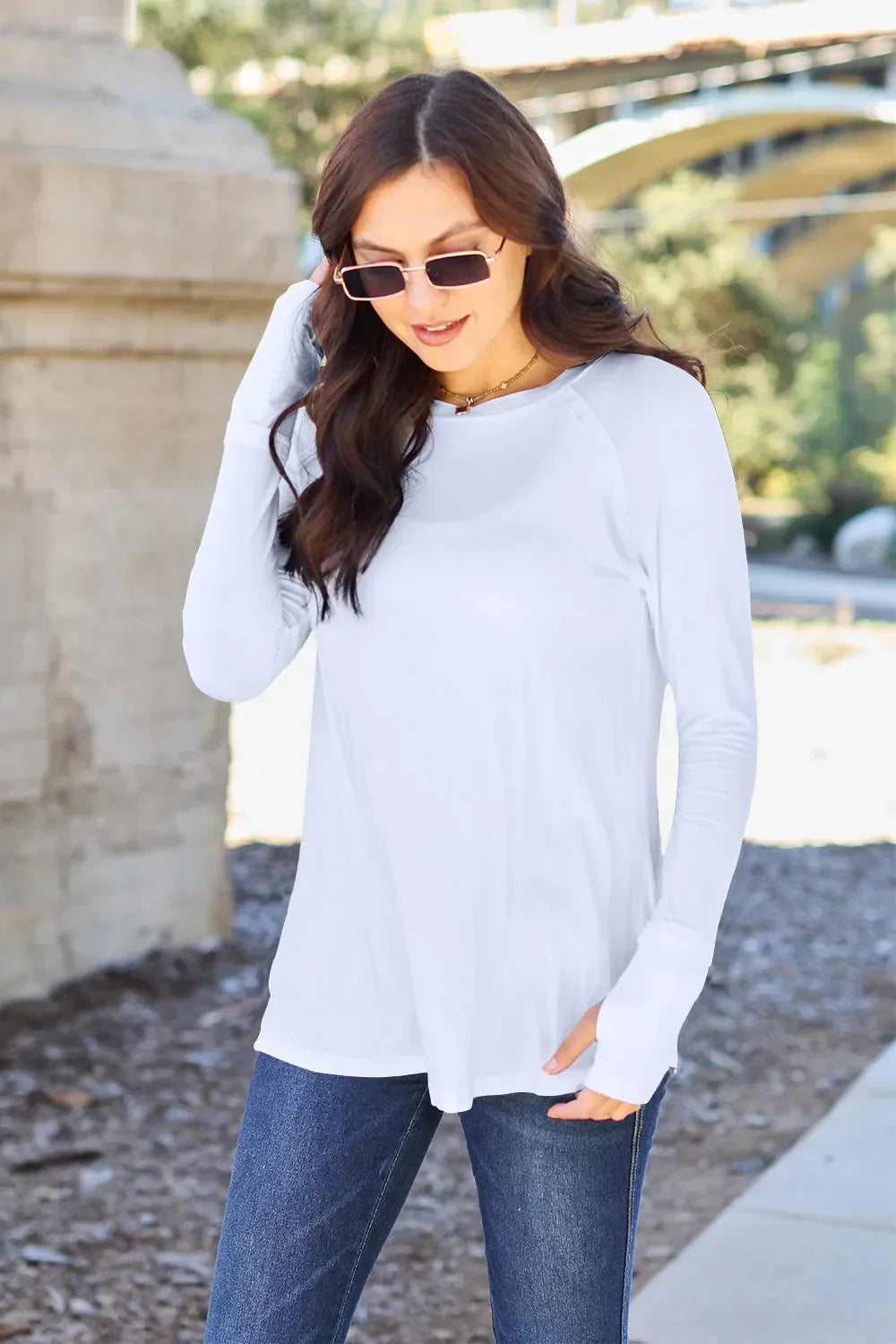 Woman in a casual white long sleeve top and blue jeans wearing sunglasses outdoors