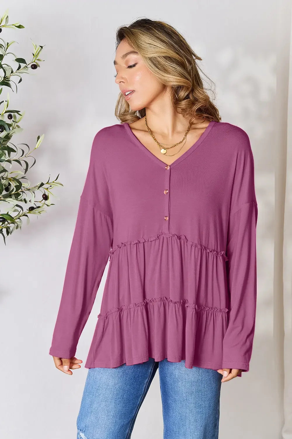 Woman wearing a mauve tiered ruffle long sleeve blouse with gold buttons and blue jeans