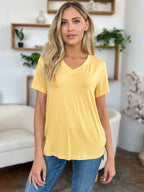 Woman wearing a casual yellow V-neck t-shirt and blue jeans, standing indoors
