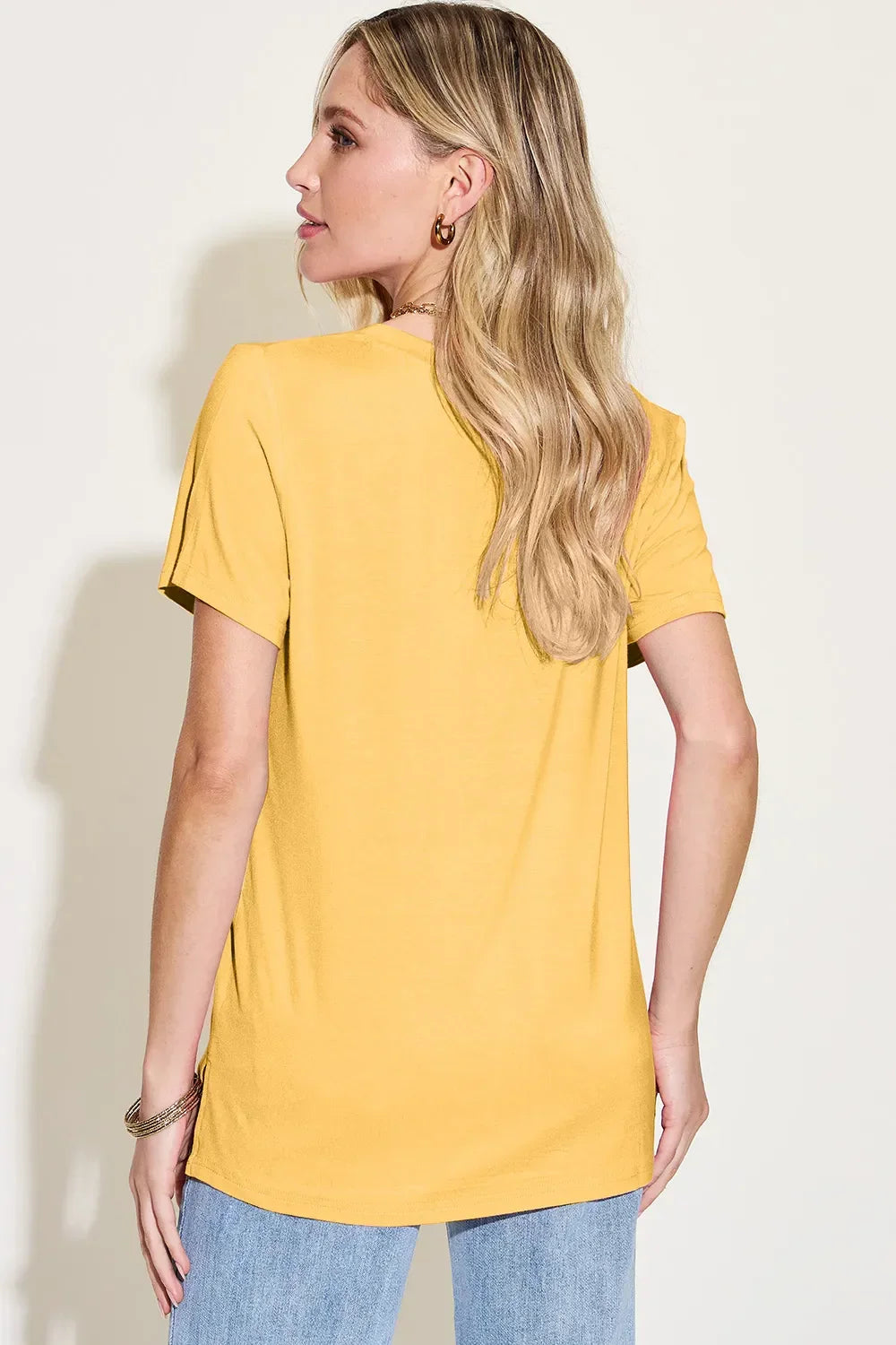 Woman in yellow short sleeve t-shirt and light blue jeans, shown from the back