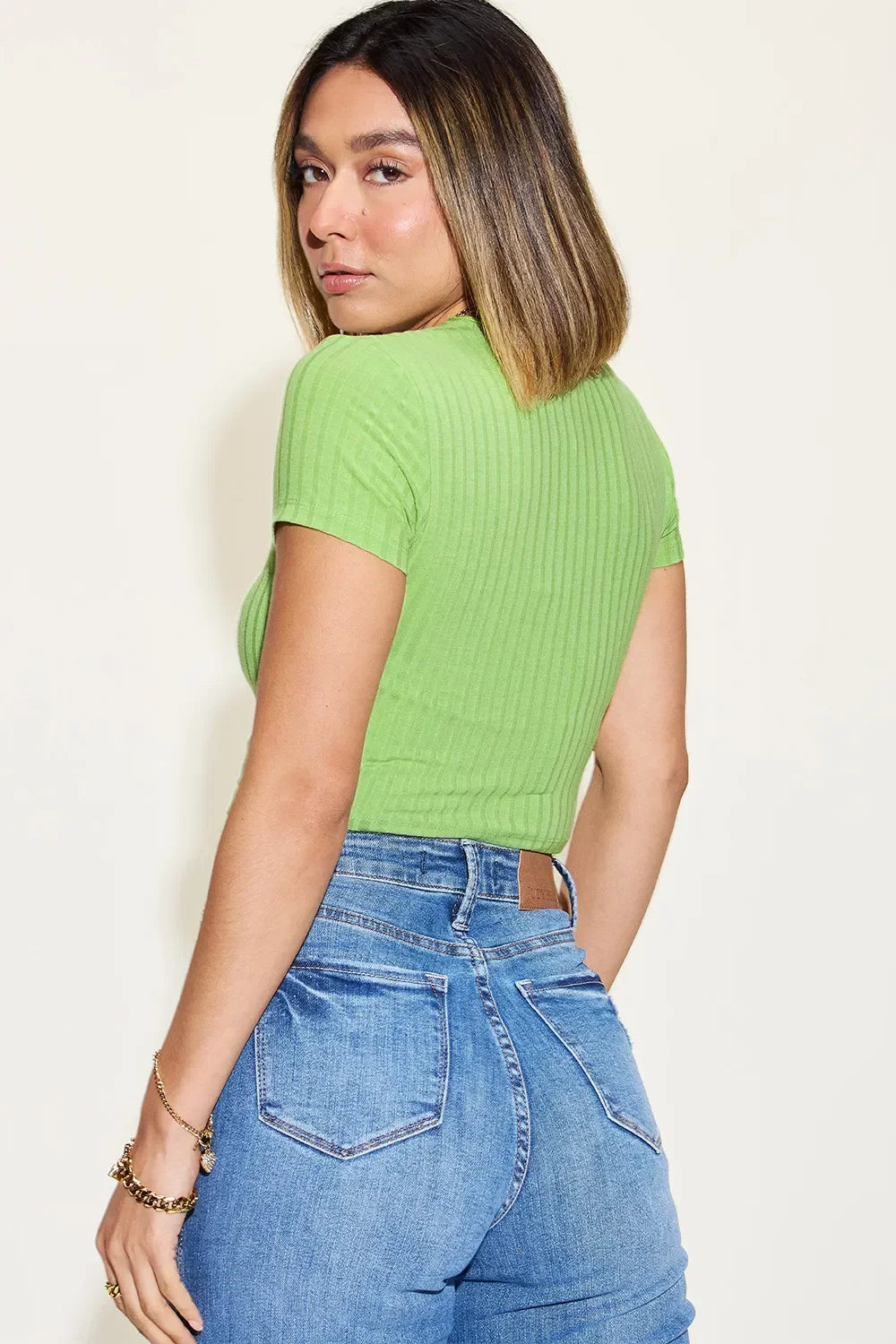 Woman wearing a green ribbed short sleeve top and high-waisted blue jeans