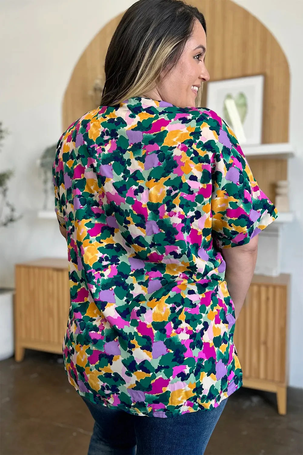 Woman wearing colorful abstract print short sleeve blouse and blue jeans indoors