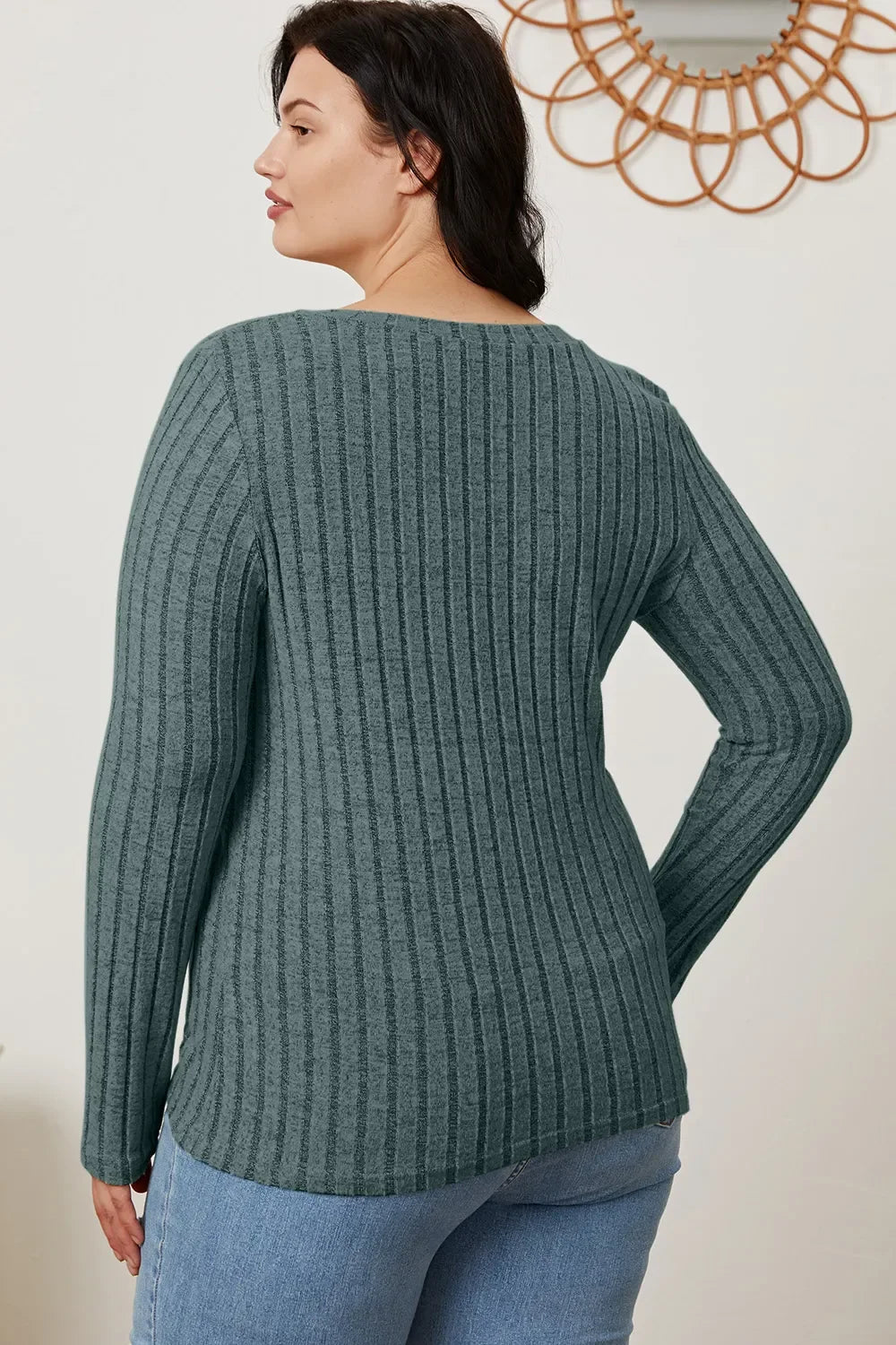 Woman wearing ribbed long sleeve green sweater and light blue jeans, back view