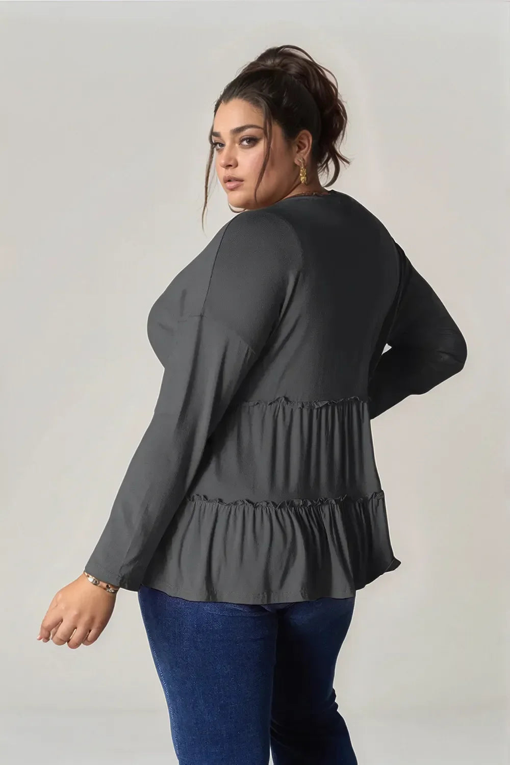 Plus size woman wearing a long sleeve black ruffle top and blue jeans, facing backwards.