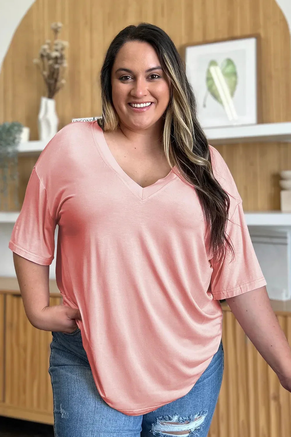 Smiling woman in a peach pink V-neck short sleeve top and ripped blue jeans