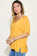 Woman wearing a loose yellow V-neck top and blue jeans, accessorized with gold jewelry