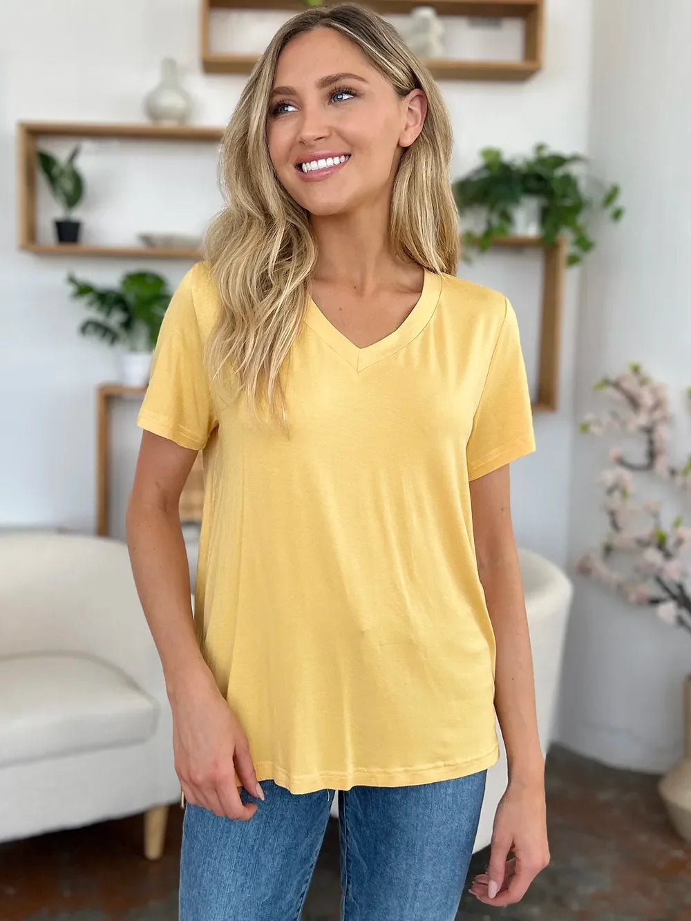 Woman wearing yellow V-neck t-shirt and blue jeans in modern living room setting