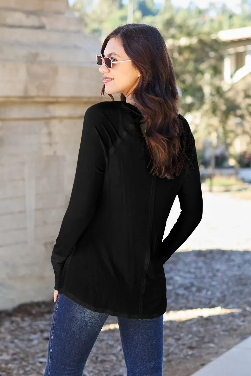 Woman in black long sleeve top and blue jeans outdoors, wearing sunglasses