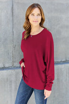 Woman in casual long sleeve red top and blue jeans standing against a concrete wall