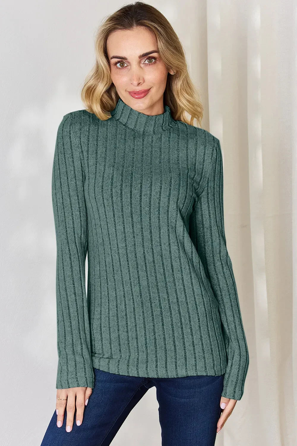 Woman wearing a green ribbed mock neck long sleeve sweater with dark blue jeans