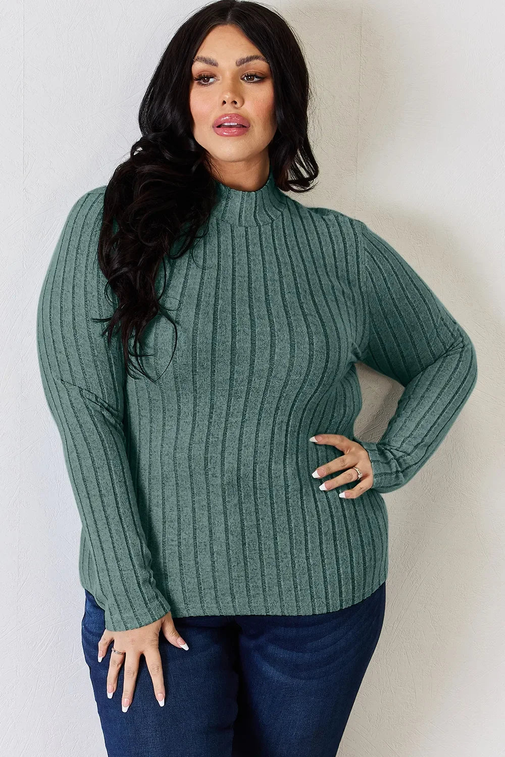 Woman wearing a green ribbed long sleeve sweater with mock neck and blue jeans