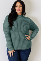 Woman wearing a green ribbed long sleeve sweater with mock neck and blue jeans