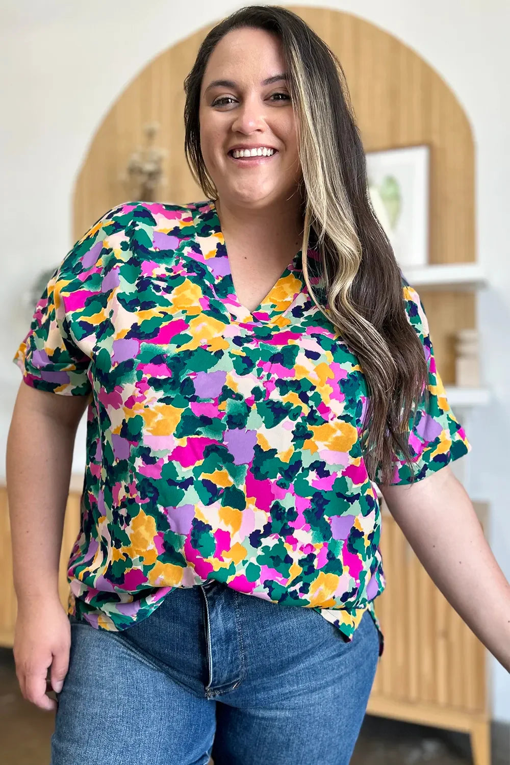 Woman in colorful abstract print blouse and blue jeans smiling indoors
