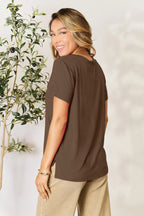 Woman modeling brown short sleeve top and beige pants near olive tree