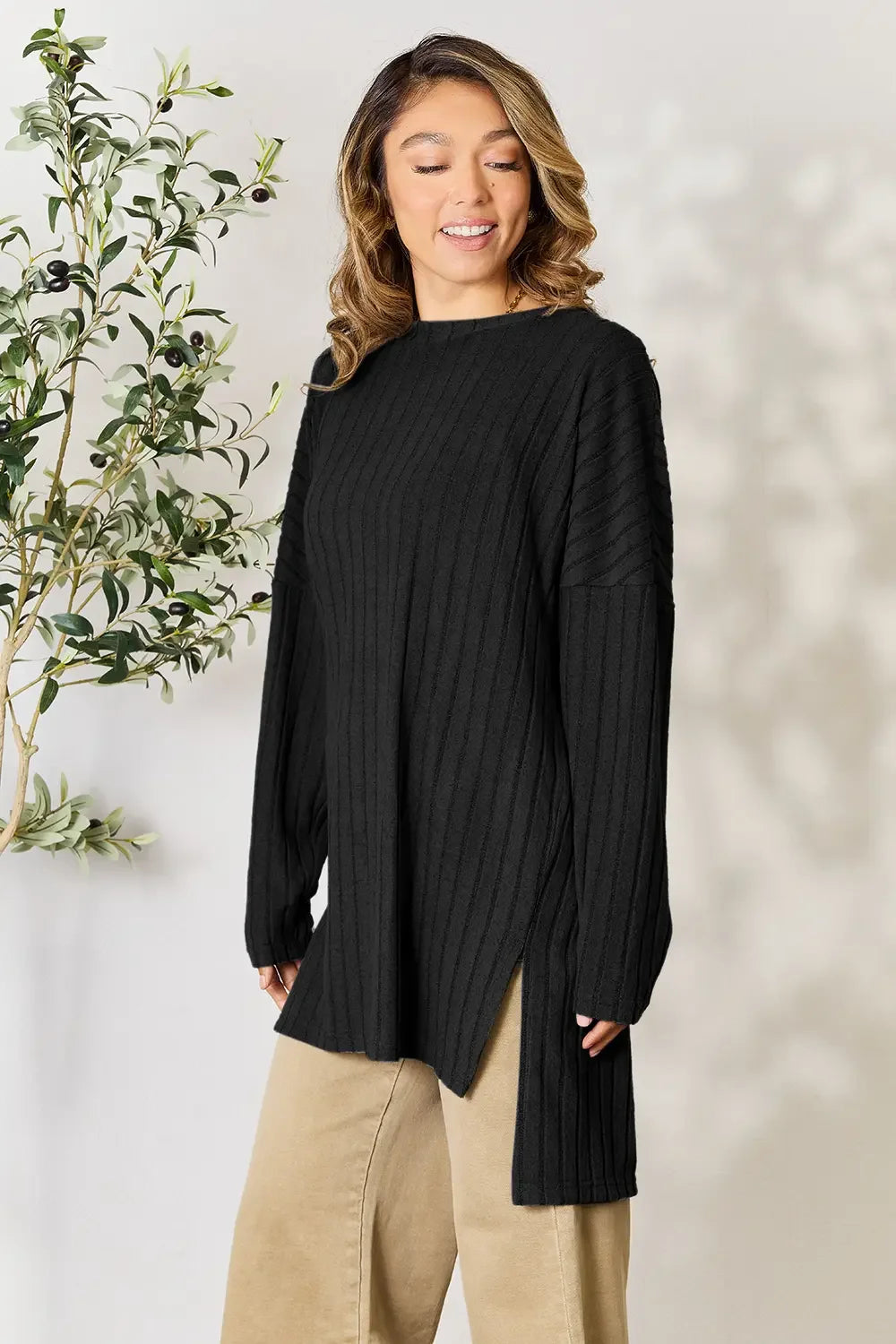 Woman wearing a black ribbed long sweater with side slits and beige pants, casual fashion