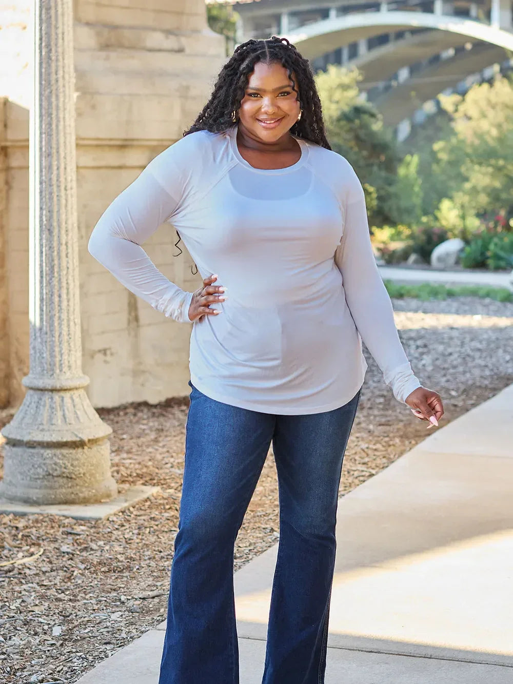 Woman in long sleeve white top and blue flare jeans posing outdoors