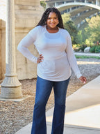 Woman in long sleeve white top and blue flare jeans posing outdoors