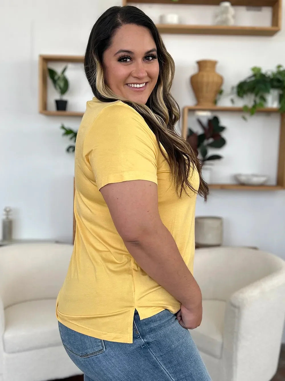 Smiling woman in a yellow short sleeve t-shirt and blue jeans in a modern living room