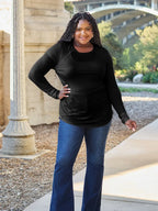 Woman in black long sleeve top and blue flare jeans posing outdoors near an archway