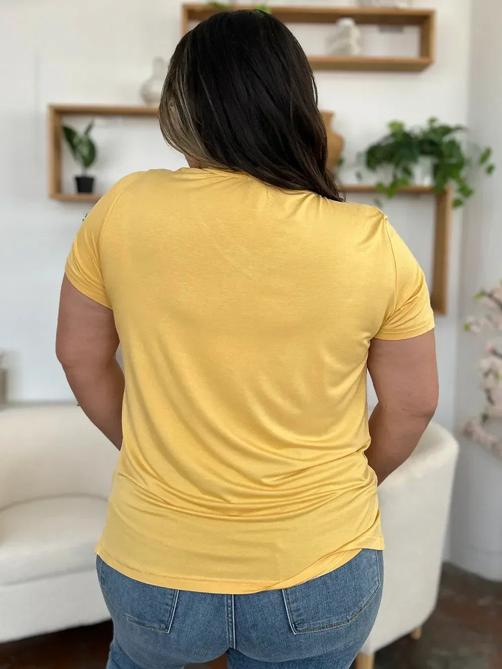 Woman in yellow short sleeve t-shirt and blue jeans, back view, casual outfit indoors