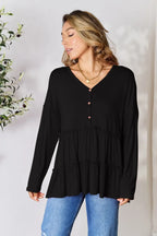 Woman wearing black long sleeve tiered blouse with V-neck and button detail, paired with blue jeans