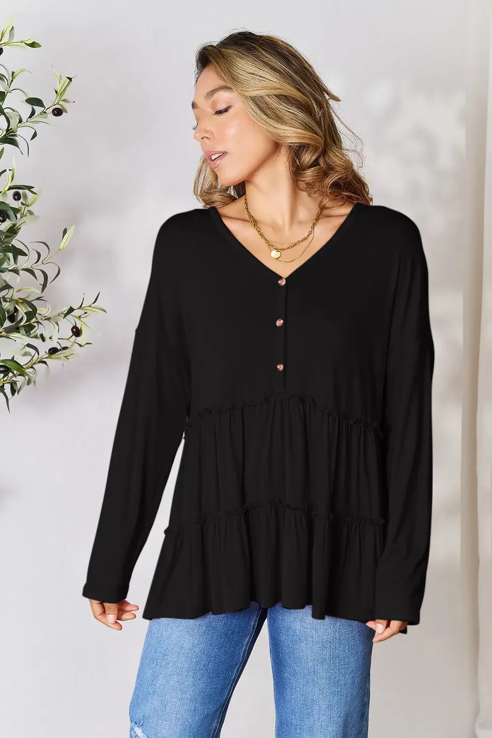 Woman wearing black long sleeve tiered blouse with V-neck and button detail, paired with blue jeans