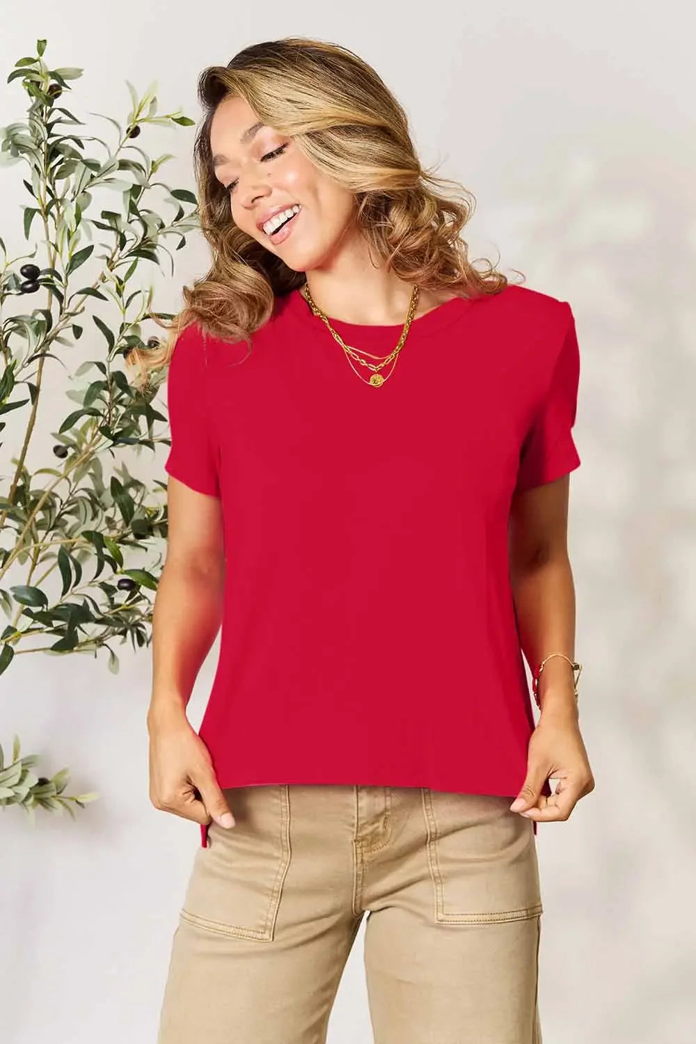 Woman wearing a red short sleeve top and beige pants, casual outfit, gold layered necklaces